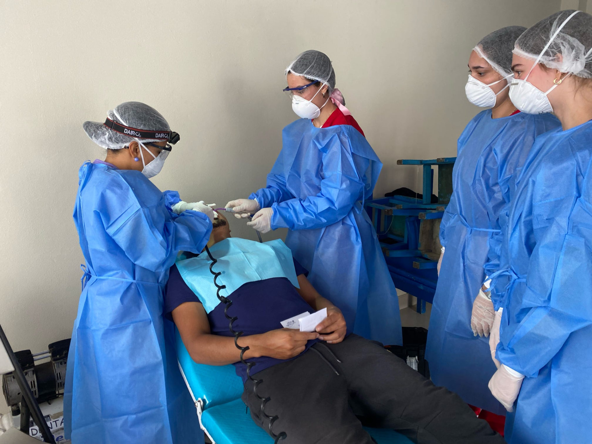 Dental practitioners in blue PPE examine a reclined patient in a bright blue dental chair at a MEDLIFE Smiles Movement mobile dental clinic near Lima, Peru